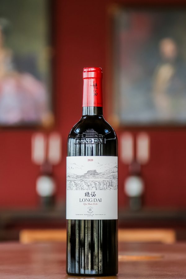 A bottle of red wine sits on a wooden table.