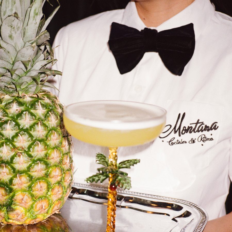 A man carries a tray with a cocktail in a palm tree glass and pineapple at Montana.