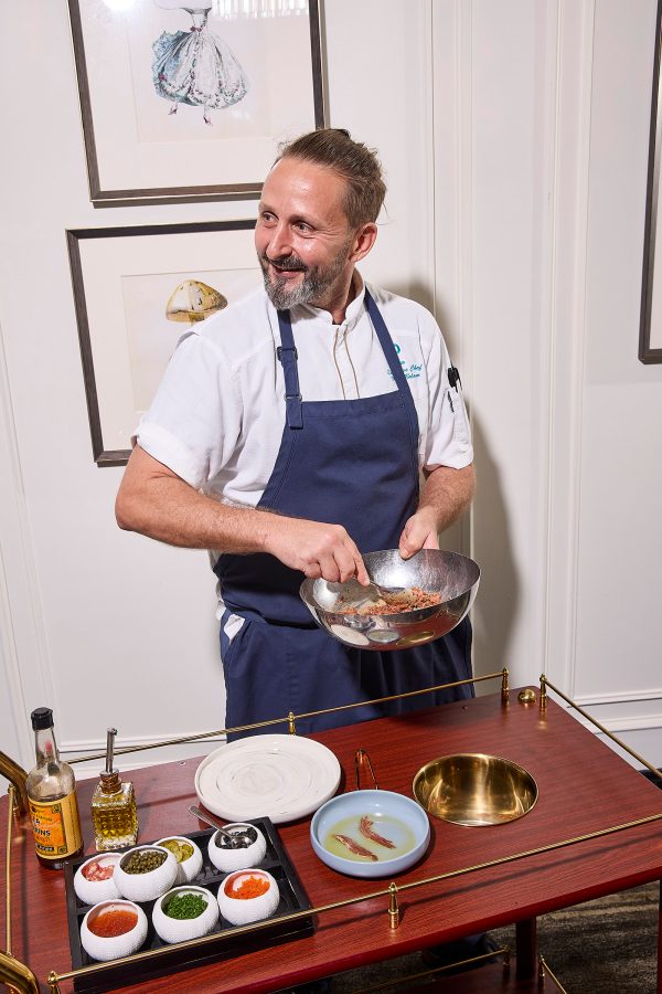 A chef at Porterhouse stirring something in a metal bowl by a wooden cart covered in sauces. 