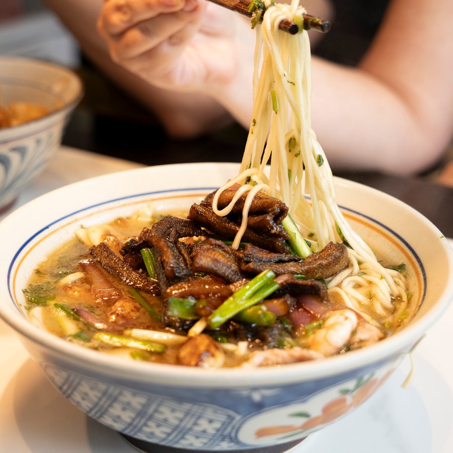 A bowl of noodle soup with preserved vegetables, bamboo shoots and sliced pork.