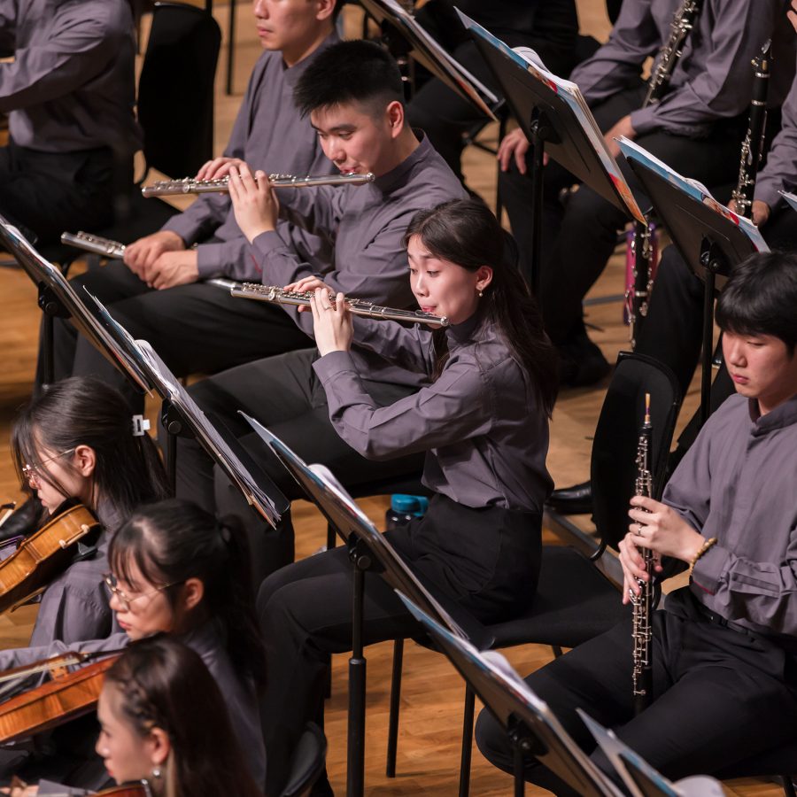 Two flautists from the Asian Youth Orchestra play as fellow members sit beside them.