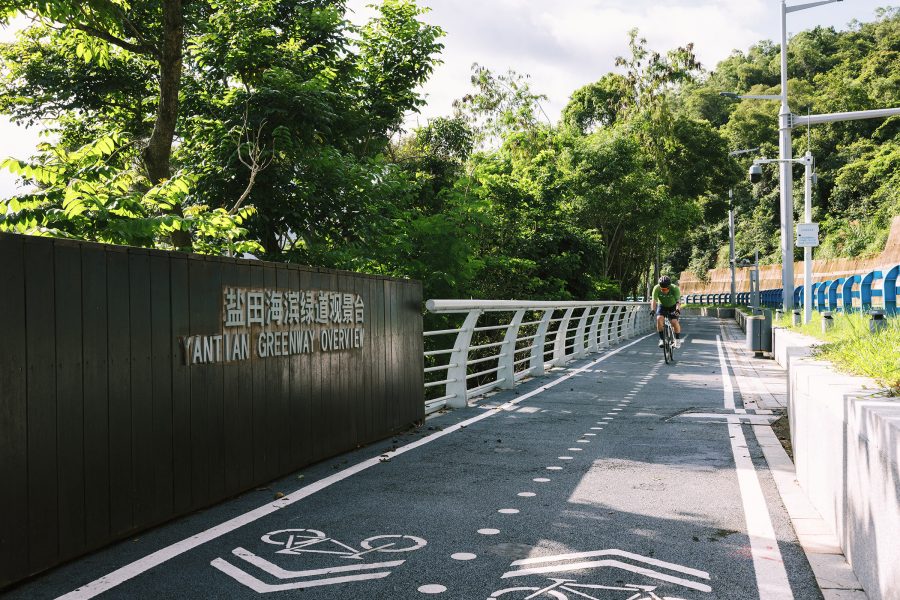 A cyclist wearing a helmet and green shirt riding his bike on a sunny day at Yantian Greenway Overwiew cycling path in Xiaomeisha, Shenzhen