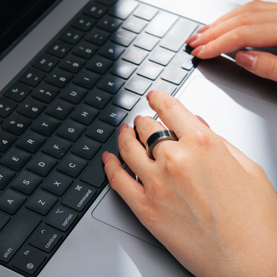 Close-up of hands on a laptop keyboard, with Momax's 1-Sense Smart Ring on the left hand’s middle finger. 