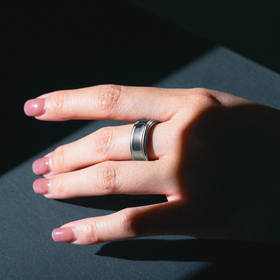 An outstretched hand against a dark surface, with Momax's 1-Sense Smart Ring on the middle finger. 