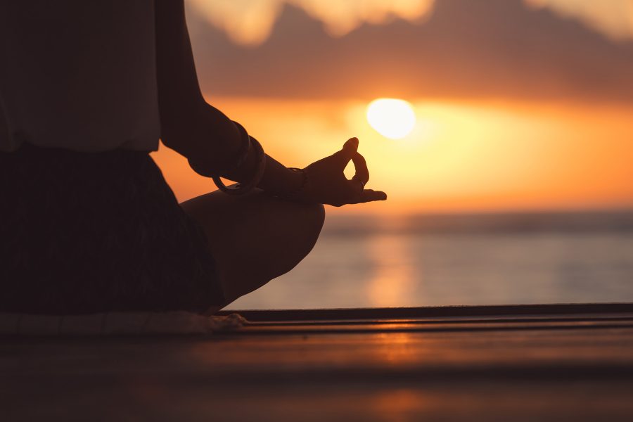 Person meditating and sitting down in front of a sunset.