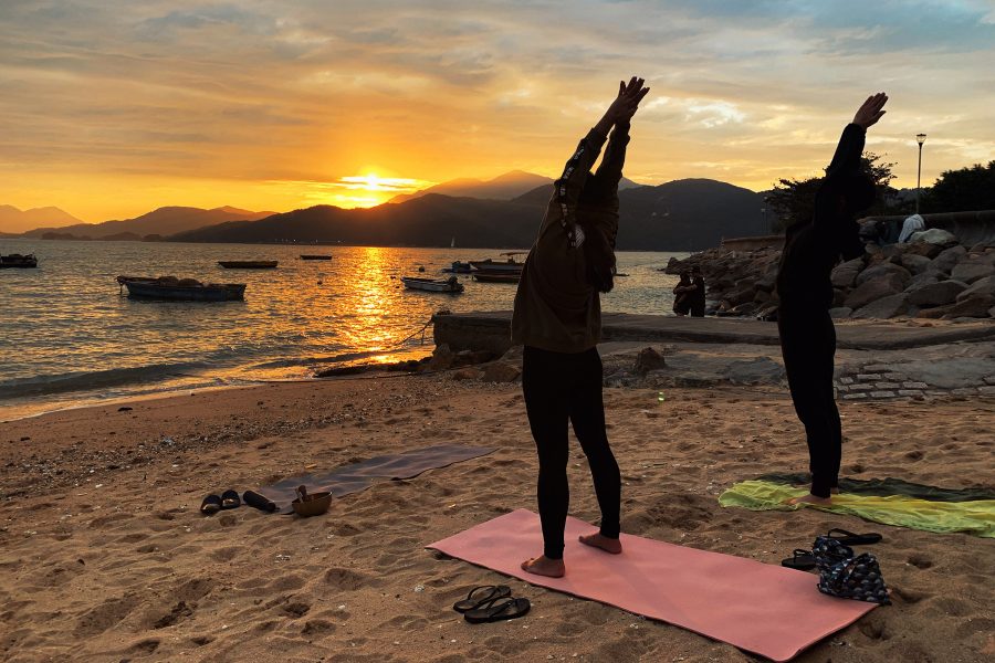 Two people doing yoga on a beach at sunrise.