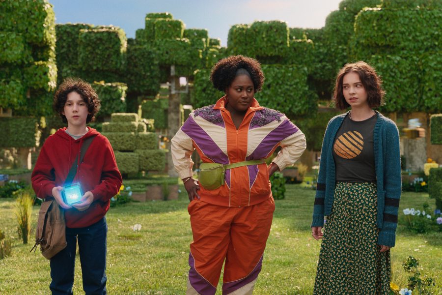 In a scene from A Minecraft Movie, a woman and two teenagers stand in a bright garden of cube-shaped trees.
