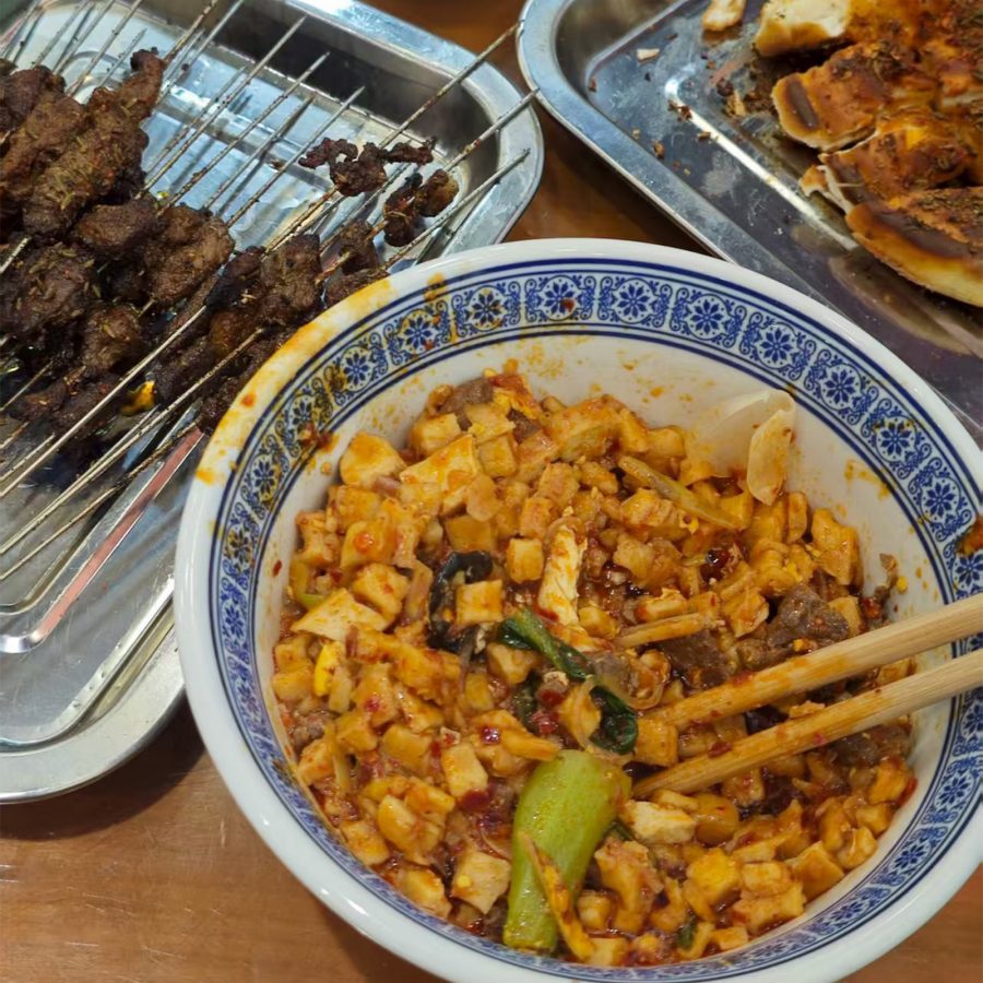 Close up on a bowl of stir-fried flatbread in Xi’an alongside meat skewers.