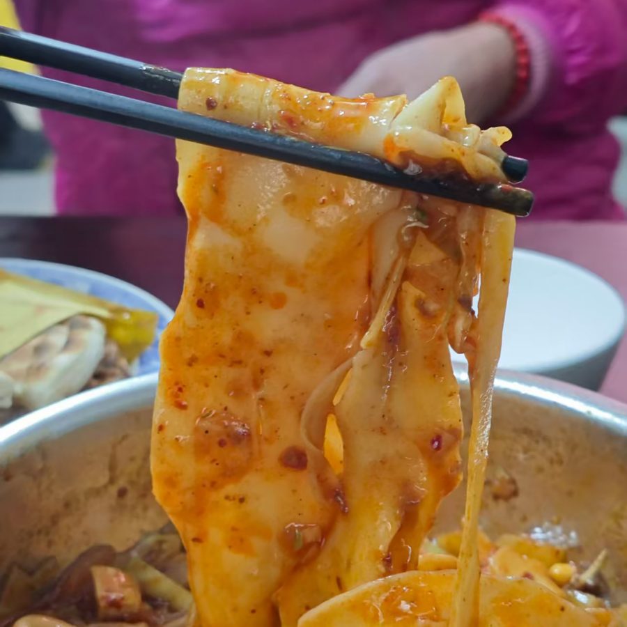 Person holding up thick strands of Youpo mian noodles in a restaurant in Xi’an.