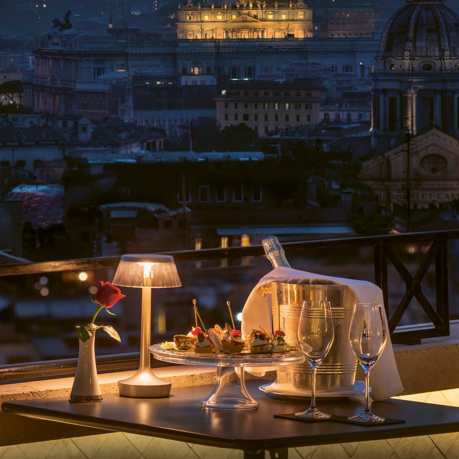 A table laid with wine and nibbles on a rooftop that looks onto the city of Rome at night. 