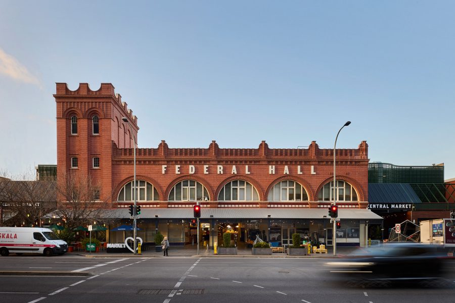 A long rust-coloured building labelled Federal Hall – Adelaide Central Market –stands on the side of the road in Adelaide. 