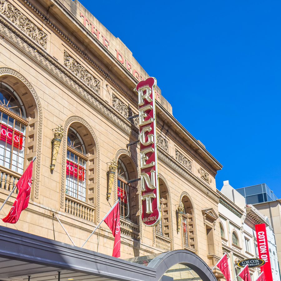 The exterior of Rundle Mall is beige with hanging signs and flags. 