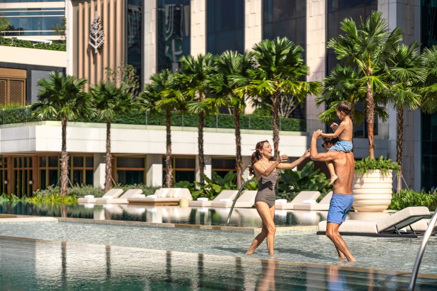 A family with young boy playing in the outdoor swimming pool of the Four Seasons Hotel Bangkok at Chao Phraya River.