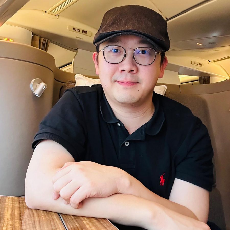 A smiling Cathay Diamond member wearing a navy polo top sits in Business class on a Cathay Pacific aircraft