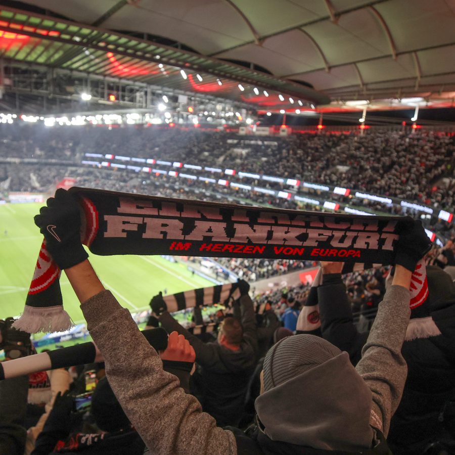 Interior view of a football match featuring Eintracht Frankfurt, with a fan holding the team’s scarf.