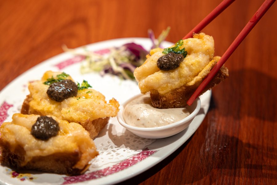 A diner picks up a fried piece of food and dips it in sauce at Sik Faan Co.