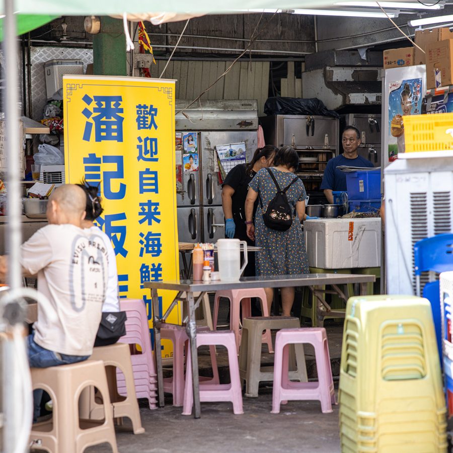 Two diners eat in front of Pun Kee’s store banner. 