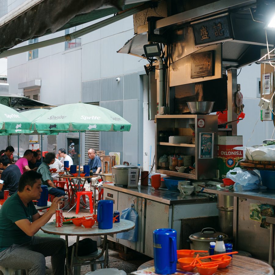 Diners eat outdoors on red plastic stools underneath green parasols at Sing Kee.