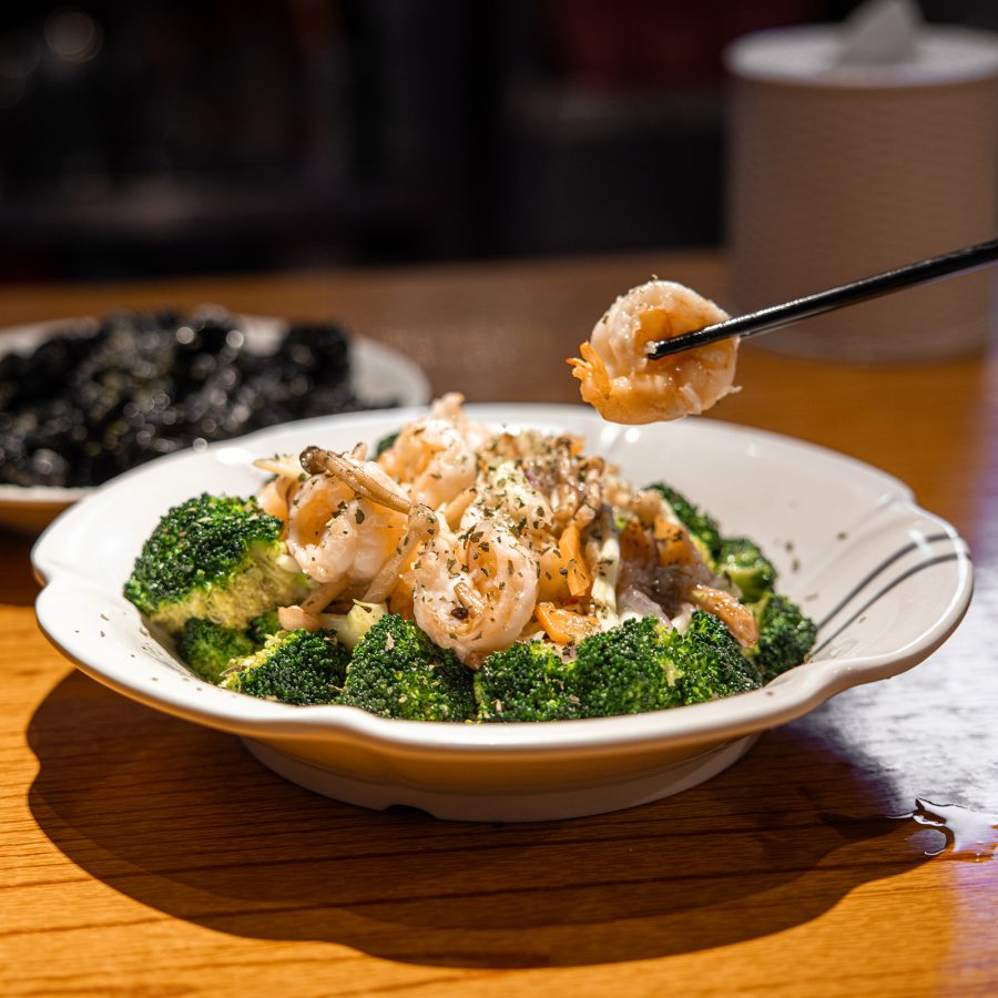 A diner picks up a shrimp from a broccoli shrimp dish with chopsticks at Tung Po Kitchen.