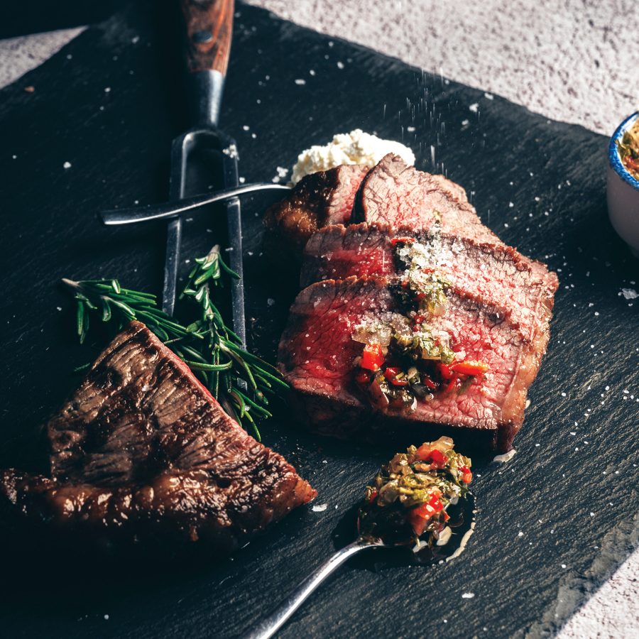 A steak, sliced and garnished with chimichurri sauce on a black ceramic plate, served at Tango Argentinian Steakhouse in Hong Kong