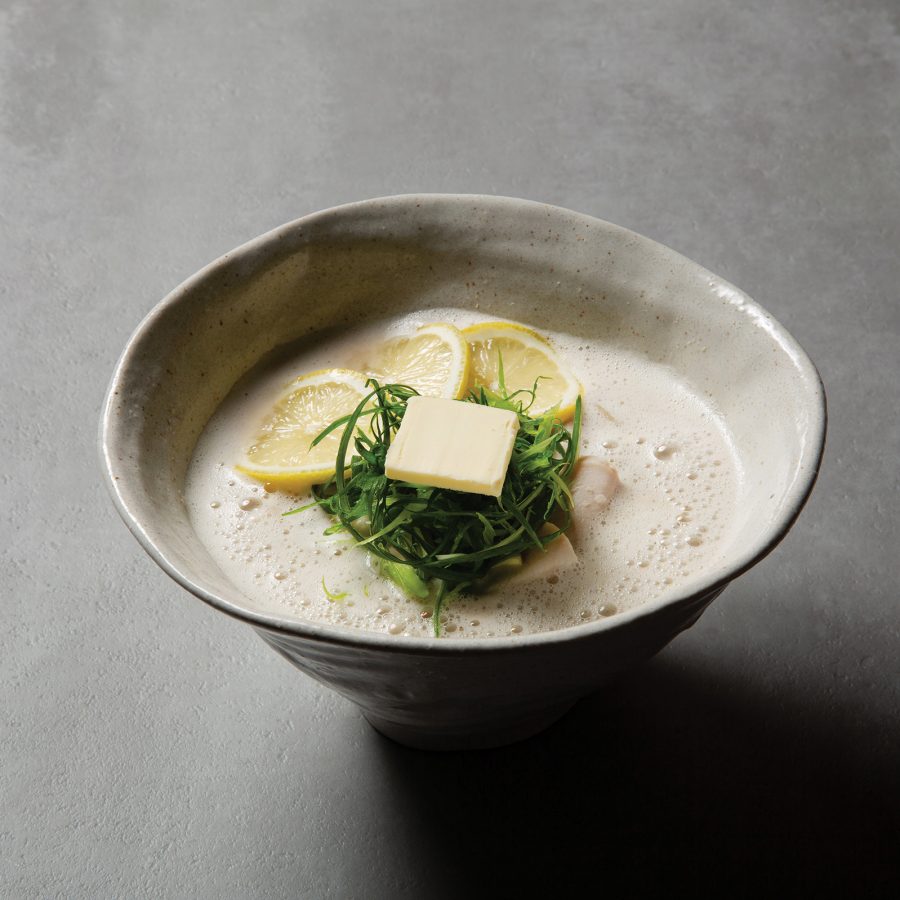A creamy chicken soup noodles in a grey ceramic bowl, garnished with lemon and herbs, served at Tsukiyomi Tori-Soba in Hong Kong