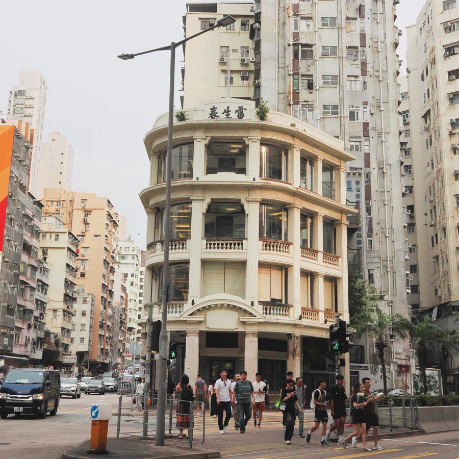 A tong lau stands on the corner of a street as pedestrians pass by below.