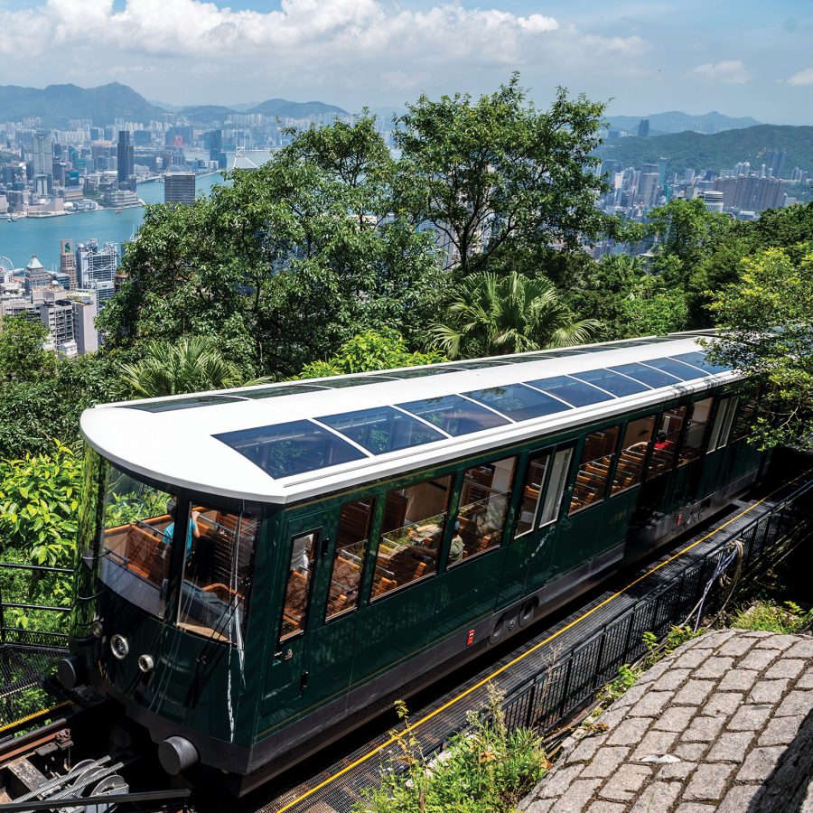 The Peak Tram climbs up the mountain with the skyline and harbour of Hong Kong visible below the treeline.