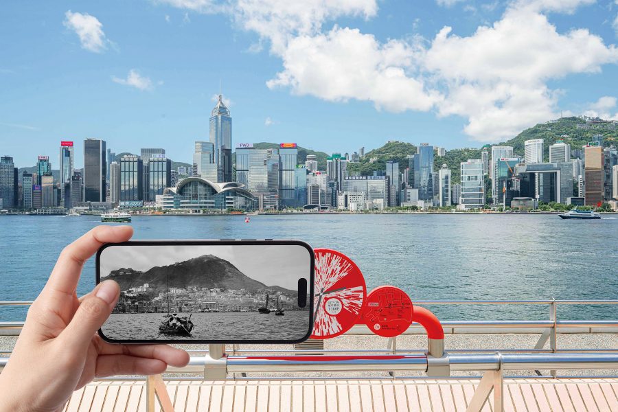 A person holds up a smartphone using the City in Time app on the skyline of Hong Kong Island to see a version of the same scenery from the past in black and white.