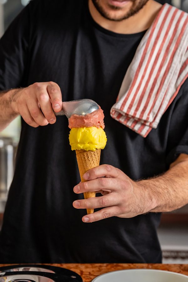 A person scoops a ball of ice cream onto a cone at Ciccone & Sons gelateria.