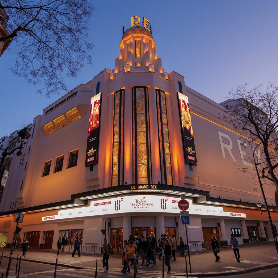 The exterior of Le Grand Rex towers over the streets in Paris at night.
