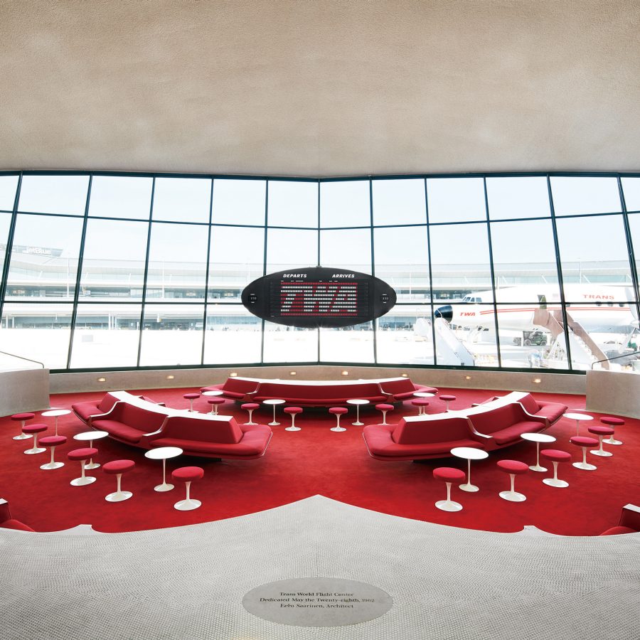 The lobby of TWA Hotel is filled with red chairs and looks out at the runway.