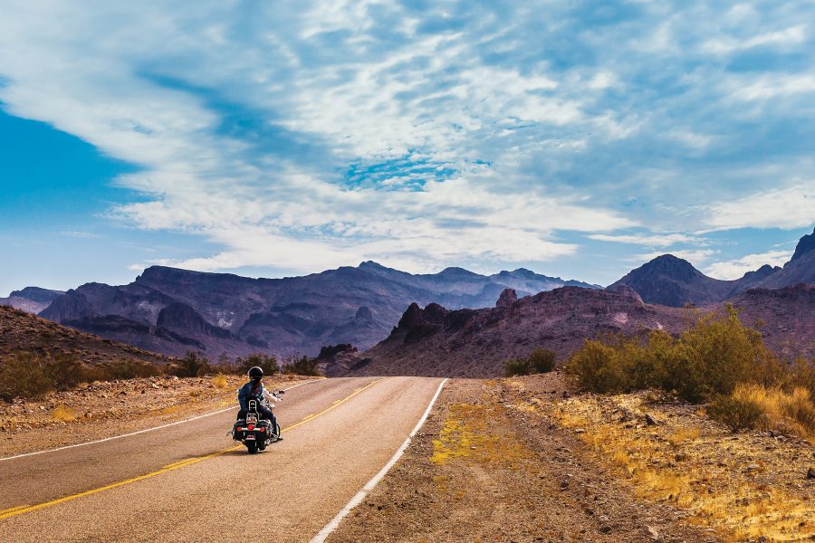 A person riding a motorcycle on Route 66, with mountains in the distance.