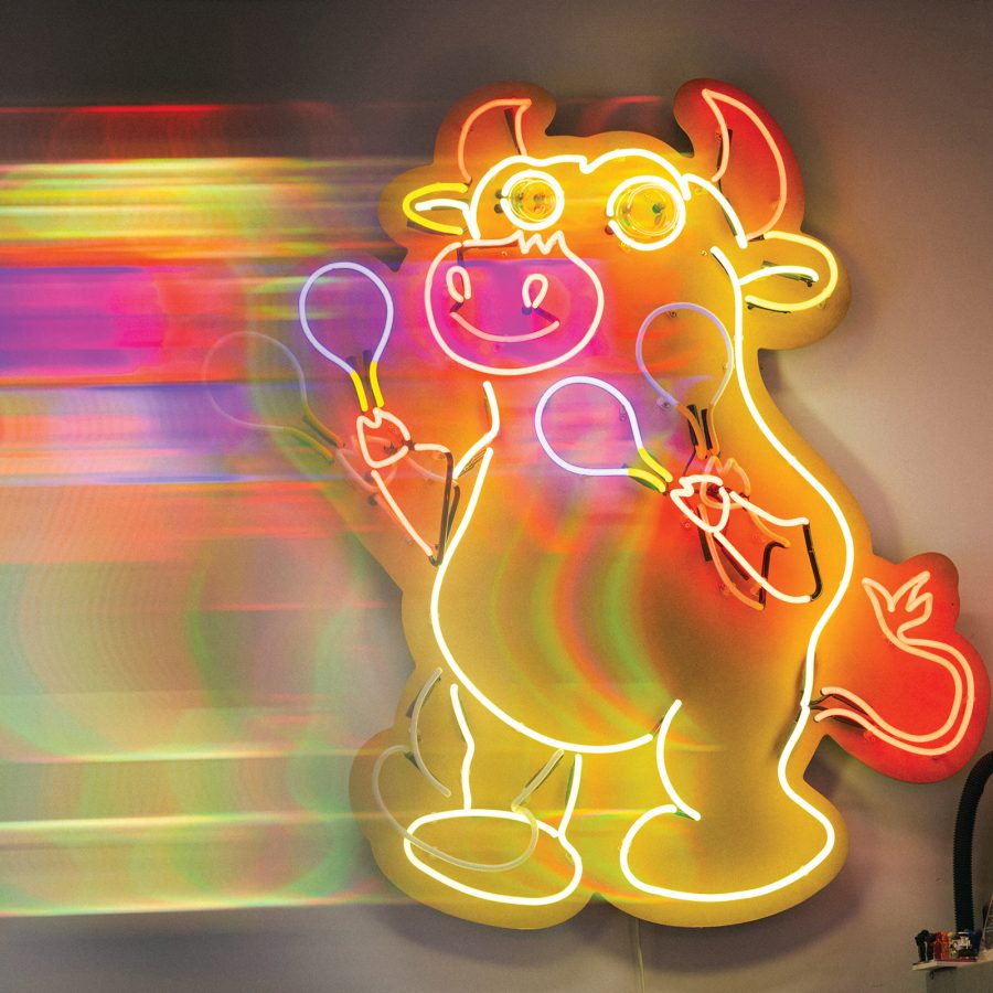 A multicoloured neon cow sign by Kowloneon, glowing on a wall