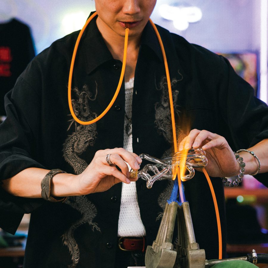 Jive Lau blowing into a glass tube while melting and shaping a neon sign in his Kowloneon studio