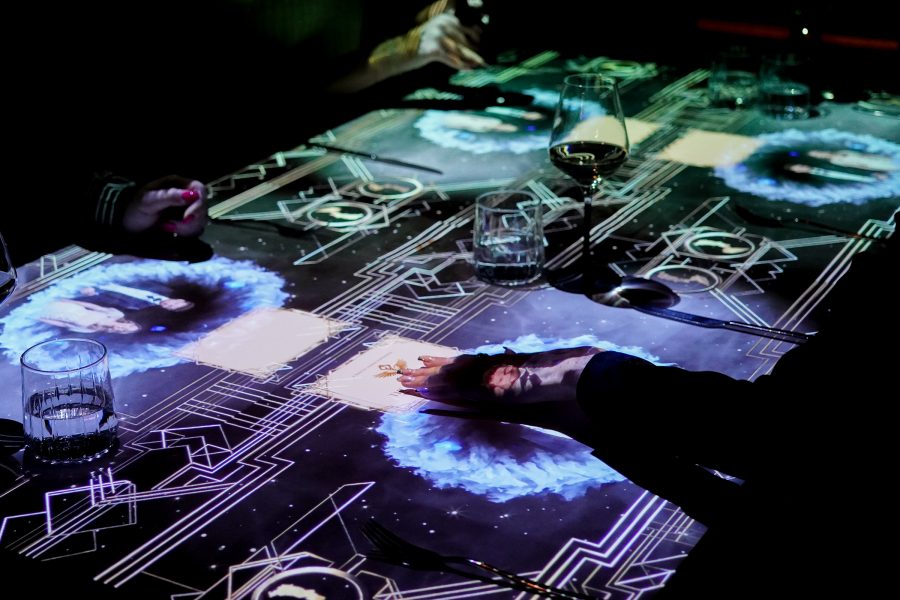 Hands with painted nails rest atop a table illuminated by an overhead projection at The Magic Table at Grand Hyatt Hong Kong.