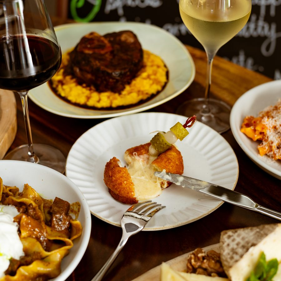 A spread of dishes at Nocino features pastas, croquettes and cheese among glasses of wine. 
