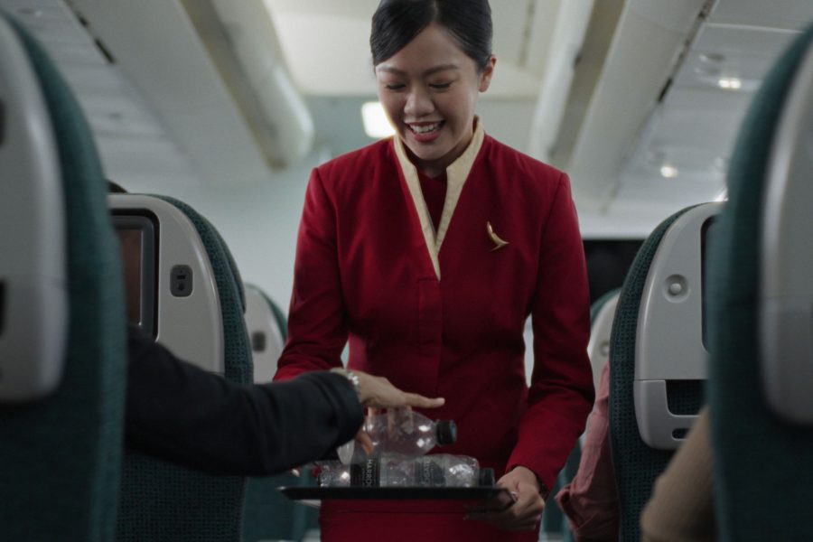 A female Cathay Pacific cabin crew holds out a tray inflight as a passenger places an empty plastic bottle onto it.