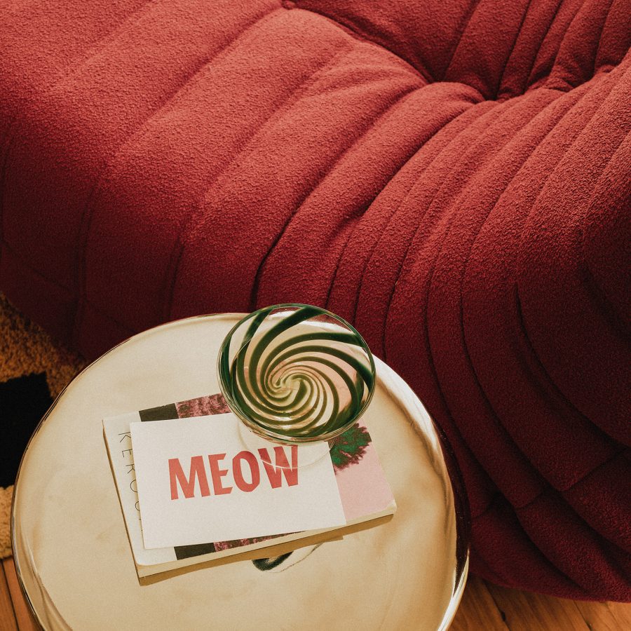 A postcard printed with the word “MEOW” on a side table by an armchair at The Cheshire Cat Motel, Gold Coast.