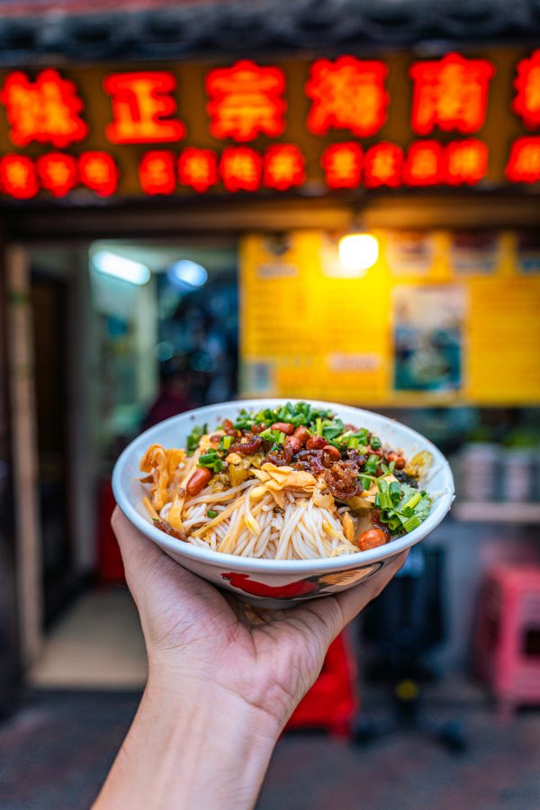 Person holds out a bowl of noodles in Yamei Hainan Rice Noodle in Haikou.