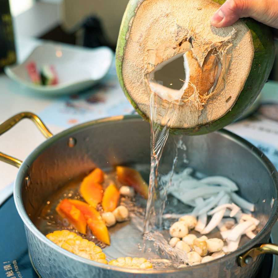 Chef pouring coconut juice into a pan of vegetables in Yexiaoji Coconut Chicken Haikou.