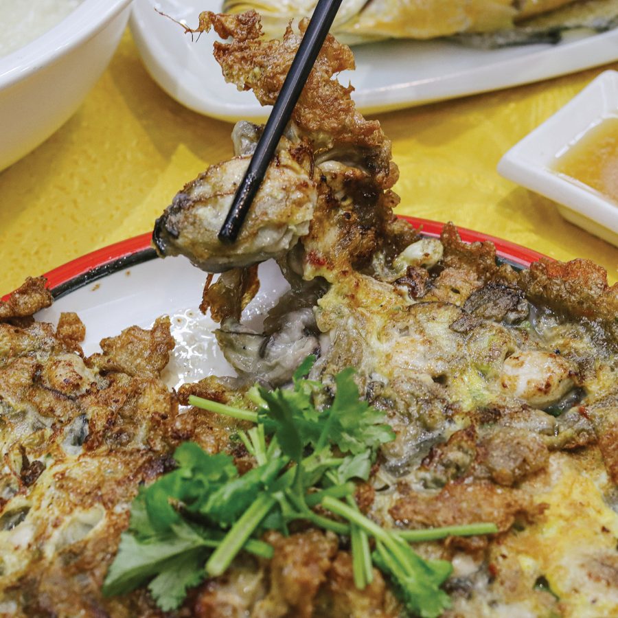 Picking up a piece of oyster omelette with chopsticks.