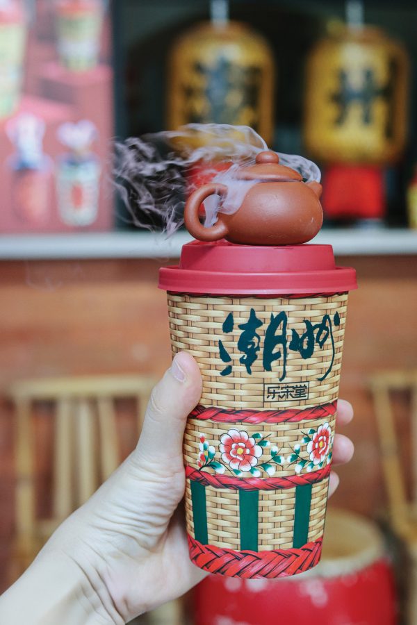 A hand holding up a takeaway cup of tea.