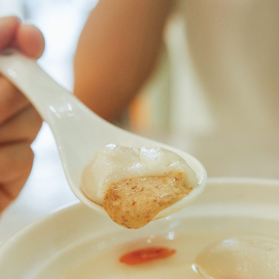 A hand holding up a peanut rice ball on a spoon.