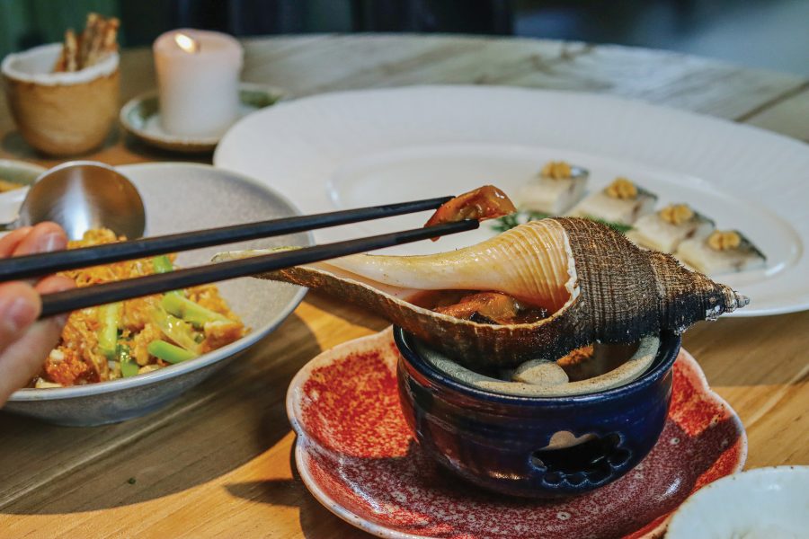 A bowl with a conch on top of it along with plates of Chaozhou delicacies.