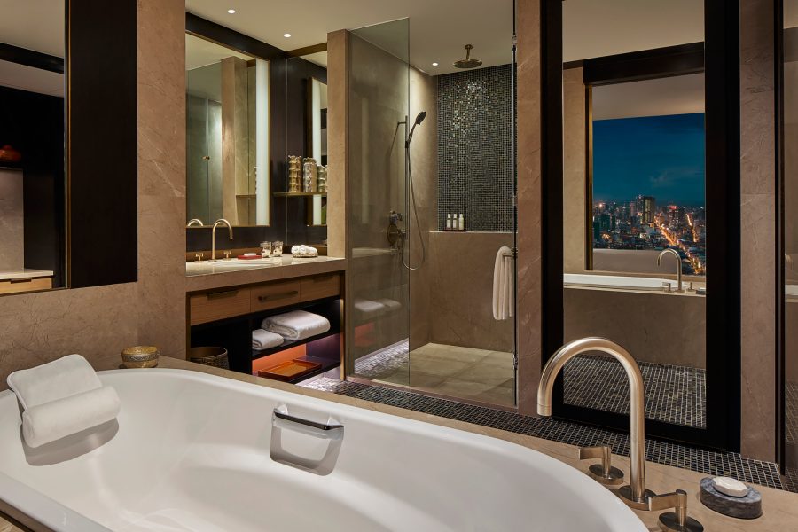A bathroom with a white bathtub, tall mirror, vanity and walk-in shower.