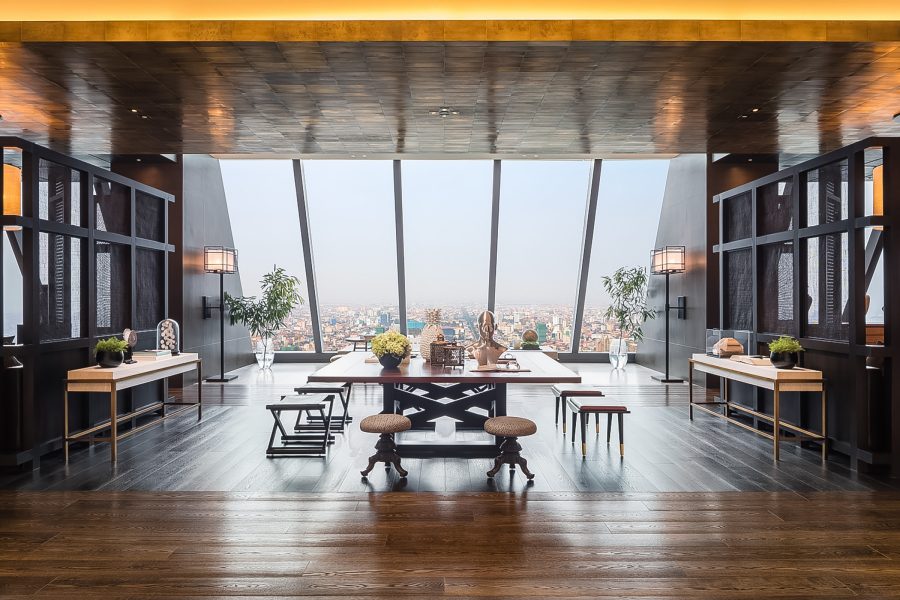 A stylish lobby with a large table surrounded by low stools and a floor-to-ceiling window looking out across Phnom Penh.