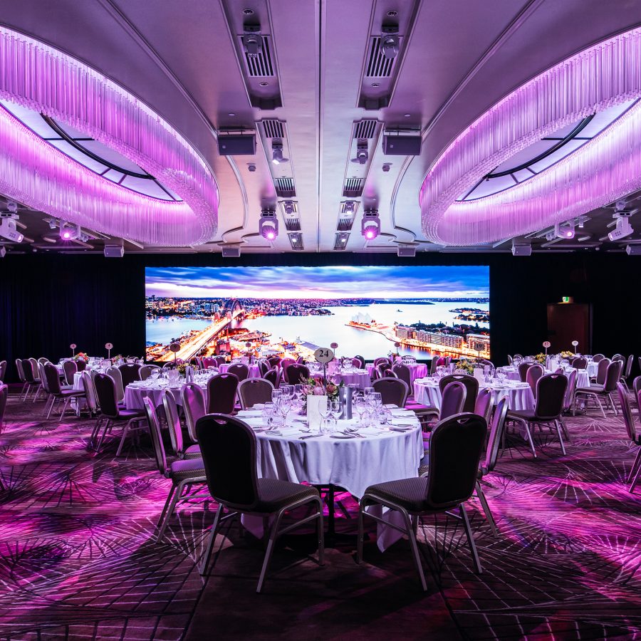 An event hall at Shangri-La Sydney is lit up in purple and occupied with round tables. 