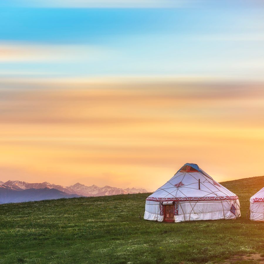 Two traditional Mongolian yurt tents on a grassland in the Xinjiang region’s Urumqi, with a view of mountains and a gradient of blue and yellow sky
