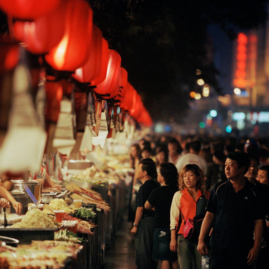 A crowd of people at Beijing’s Wangfujing Snack Street market lined with food stalls and red lantern 
