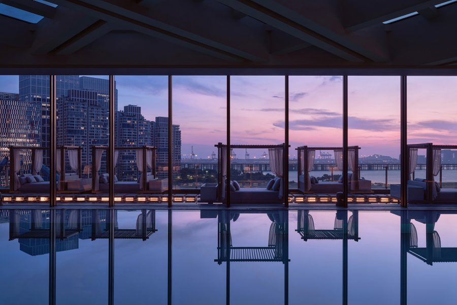 Conrad Shenzhen’s hotel pool, lined with poolside daybeds, reflects the twilight sky behind Qianhai’s skyline. 